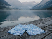 Badehose Greek Azure flach auf einem Holzsteg am Schweizer Alpensee mit Bergen und Nebel im Hintergrund