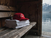 Badmeister Lifeguard Cap auf gefalteten Badetüchern in einem Schweizer Bootshaus mit Blick auf Alpensee und Berge