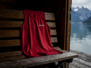 Badmeister Tanktop rot drapiert auf einer Holzbank in einem Schweizer Bootshaus mit Blick auf Alpensee und Berge