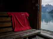Badmeister T-Shirt rot über einer Holzbank in einem Schweizer Bootshaus mit Blick auf den Alpensee und Berge